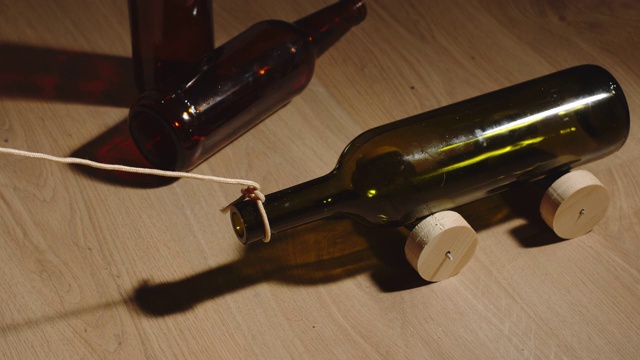 俯视图:家里地板上用绳子推着旧玻璃瓶上的玩具车视频下载