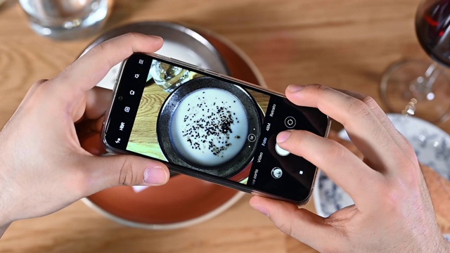 一名男子用智能手机拍摄餐馆或咖啡馆的食物。高质量的画面视频素材