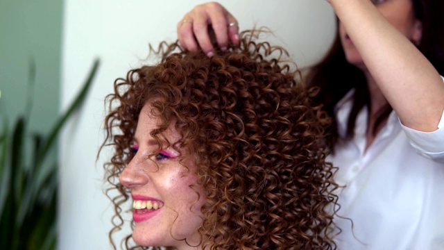 专业发型师为年轻的红发少女客户做造型。美发师做最后的触摸姜长卷发视频下载