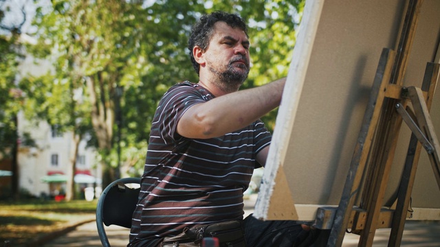 盖伊艺术家正在画布上用油画颜料画一幅画，而坐在城市公园的小巷视频下载