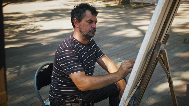 男艺术家用油画颜料在帆布上画，而坐在城市公园的小巷上视频下载