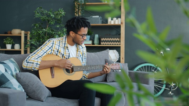 一个年轻的美国黑人在家里弹吉他唱歌的慢镜头视频素材