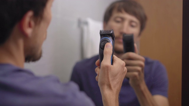 一个年轻人的特写镜头，用胡子修剪器刮他的胡子视频素材