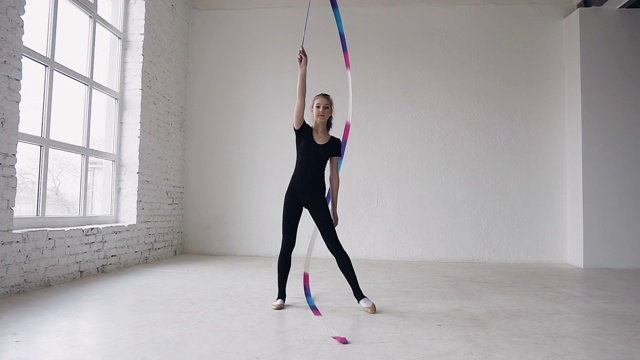 金发少女舞蹈艺术体操，现代与彩色丝带在黑色的身体在白色的背景在体育学校视频下载