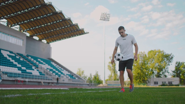 职业男子足球运动员运动员在足球场上用慢动作在运动器材上变戏法。一个足球运动员带着一个球在体育场的保持向上的看台附近视频购买