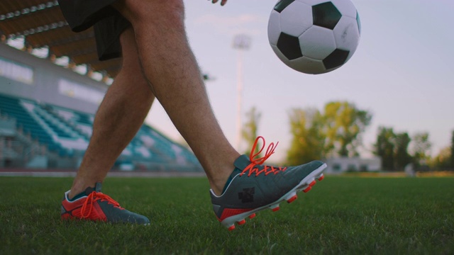 在阳光明媚的夏日，职业足球联赛男子在户外运动场上用腿抛球，用慢动作倾斜视频素材
