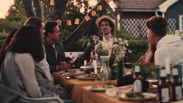 慢动作拍摄的微笑的男子与朋友聊天，而坐在桌旁的花园聚会视频素材