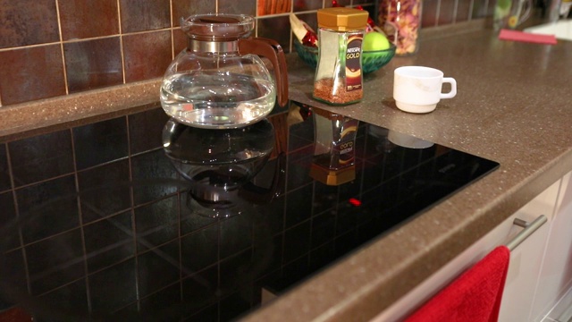 电磁炉上的水壶。炉子上的玻璃茶壶。男人把水壶放在炉子上。视频素材