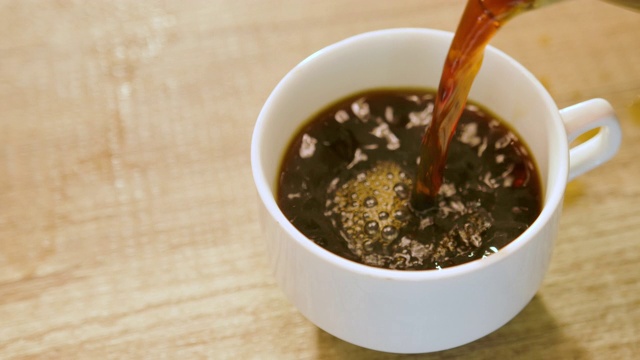 将新煮好的黑咖啡倒入白色陶瓷杯中。视频素材