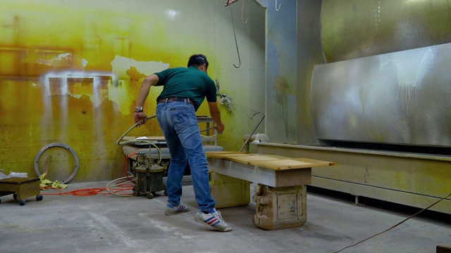 在画室里，一名男子正在用喷漆机给一件木制家具喷漆。视频素材