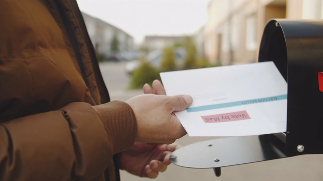 特写的人的手把信和投票选票放入一个邮箱附近的房子视频素材