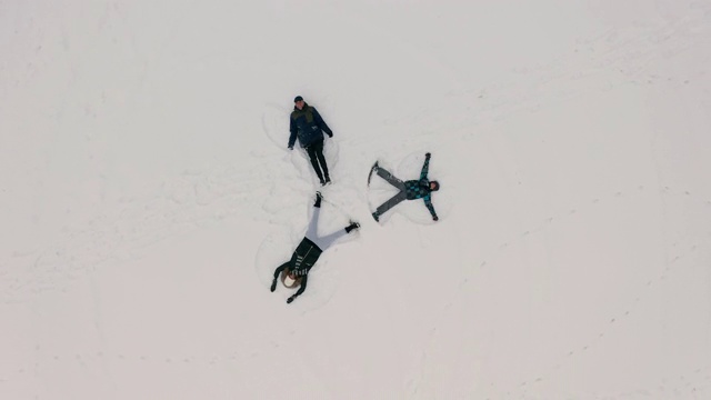 空中俯瞰快乐的三个人在寒假玩雪做天使在圣诞节假期。视频下载