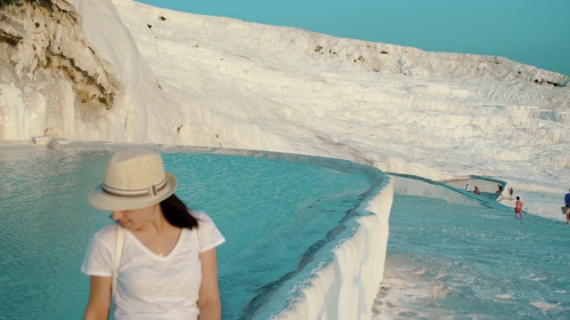 这名女游客在美丽绝伦的棉花堡石灰华中触摸着水。视频下载