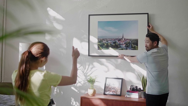 一对年轻夫妇在客厅的墙上挂一个相框视频素材