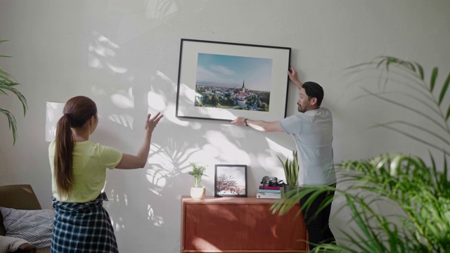 一对年轻夫妇在客厅的墙上挂一个相框视频购买