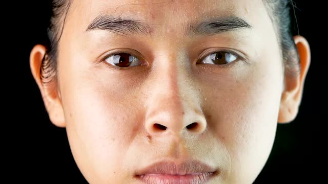 一个愤怒的亚洲女人在黑色背景上皱眉的特写。视频下载