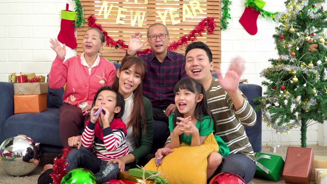 东南亚几代同堂的一家人面带微笑，对着镜头打招呼，在网上播出，从装饰着圣诞树和装饰品的家里开始了新的正常生活。儿子和女儿感觉兴奋的圣诞礼物是什么。视频下载