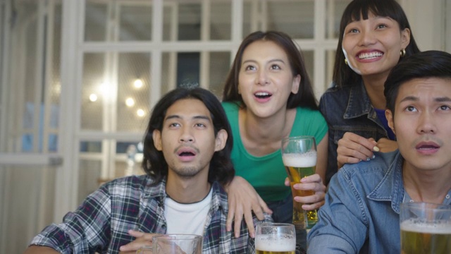 跟踪拍摄:年轻有魅力的亚洲朋友男女在夜店或家中在线观看体育比赛，心情激动，心情愉快，享受胜利时刻。快乐击掌掌。视频素材