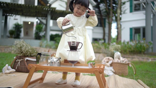 一个快乐的蹒跚学步的小孩正在花园里煮咖啡。视频下载