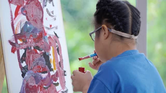 10岁亚洲唐氏综合症女童，戴眼镜在纸板上画水彩画，居家预防冠状病毒或新冠肺炎疫情。家庭教育和远程教育的概念。视频下载