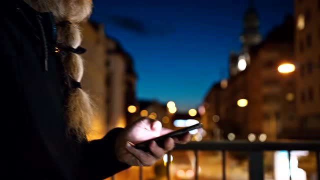 一个留着长胡子的男人在晚上走在城市里用智能手机视频素材