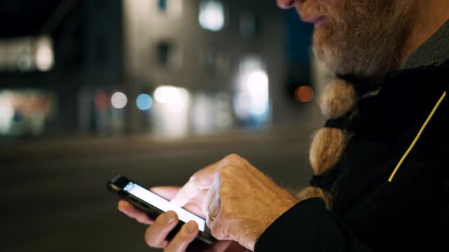 留着长胡子的男子晚上在城市的人行道上用他的智能手机视频素材