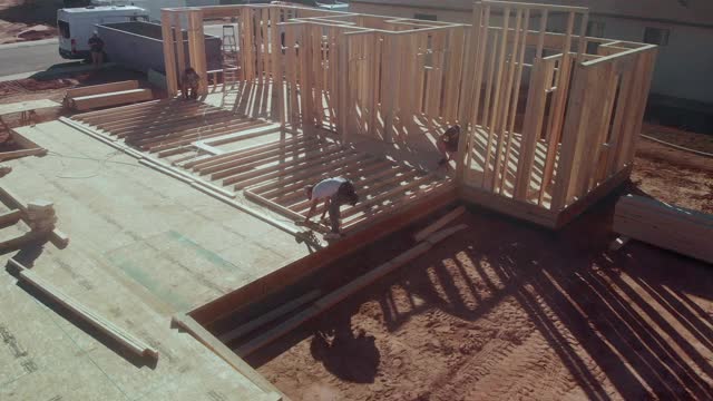一名年轻的木匠建筑工人正在工地上建造一所住宅，他正在用气枪将一堵木框墙垂直地竖起来视频下载