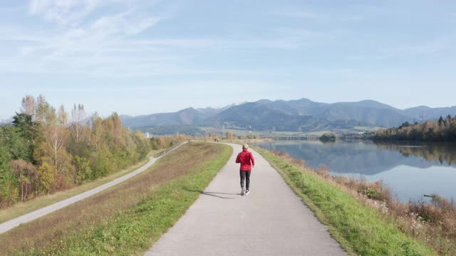 身着红色长袖衬衫的男子在以山为背景的柏油路上奔跑。运动的人的活动和健康的生活方式4K概念镜头。视频素材