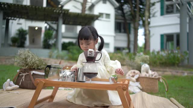 一个快乐的蹒跚学步的小孩正在花园里煮咖啡。视频素材