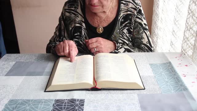 老妇人在读圣经，脖子上挂着圣母玛利亚的金章。视频下载