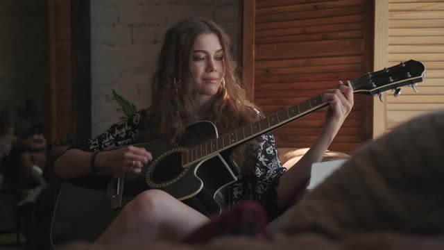 一个女人在练习弹吉他，弹着和弦，坐在窗边视频下载
