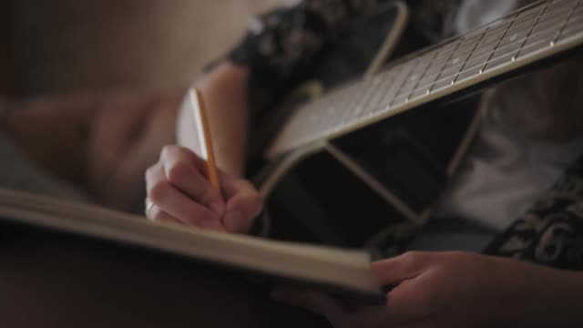一个女人弹吉他，停下来，在笔记本上写下文字或笔记视频下载