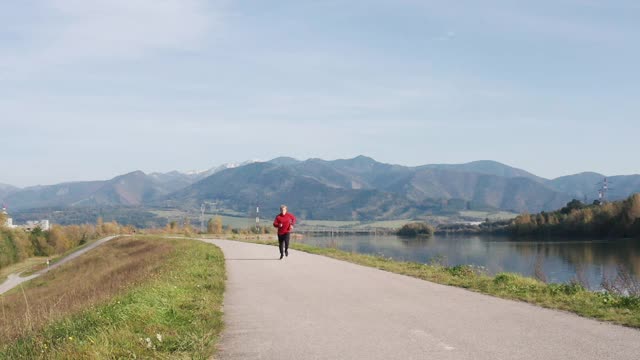 慢镜头:一个穿着黑色运动裤和运动衫的男人在山的背景下跑步视频素材