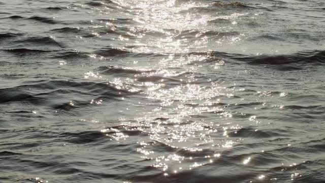 手持式相机滑动水面与太阳反射波缓慢运动。飞过湖面，反射着明亮的阳光。海洋壁纸自然度假旅游视频素材