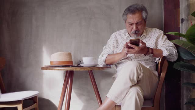 肖像的亚洲高级男子使用智能手机，而坐在咖啡店咖啡厅，高级男子打字短信和工作移动设备，人们的生活方式技术概念视频下载