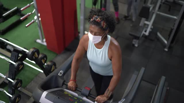 高角度的一个高级妇女在跑步机上在一个健身房-使用面罩视频下载