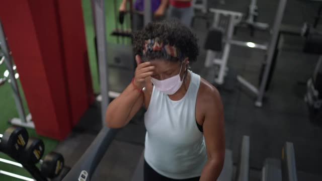 老年妇女使用跑步机在健身房使用口罩视频素材