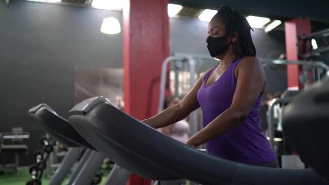 成熟的女人使用跑步机在健身房与教练的支持-使用面膜视频素材