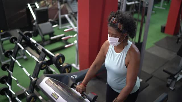 年长的妇女在教练的帮助下在健身房使用跑步机-使用面罩视频素材