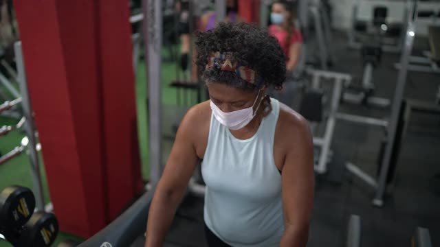 老年妇女使用跑步机在健身房使用口罩视频素材