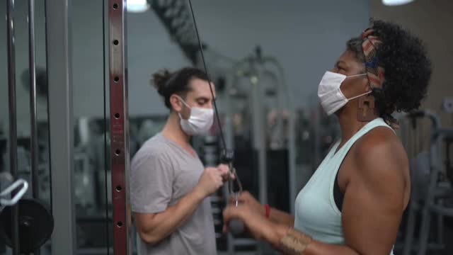 私人教练帮助老年妇女在健身房做运动-使用口罩视频下载