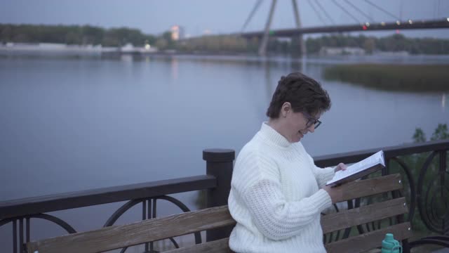 一个女人坐在公园的长椅上看书。阅读和休息。视频素材