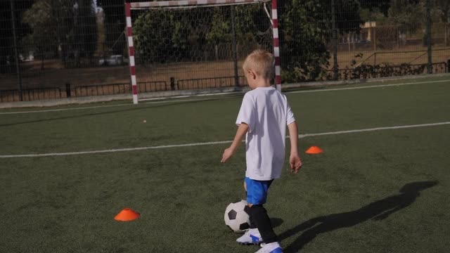 一个小男孩在足球场上训练，他练习运球和射门。视频下载