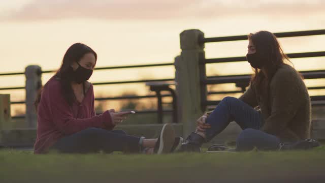 两个戴着防护面具的女性朋友坐在户外的草地上聊天视频素材