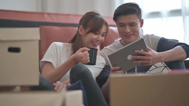 亚洲华人夫妇坐在地板上休息后打开纸箱纸箱在客厅搬家视频下载