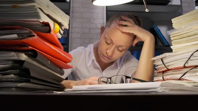 疲惫的商务女性在晚上处理文件时坐在办公室的桌子上睡着了视频素材