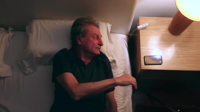 男人晚上在床上看手机，俯视图。老年人使用智能手机视频下载