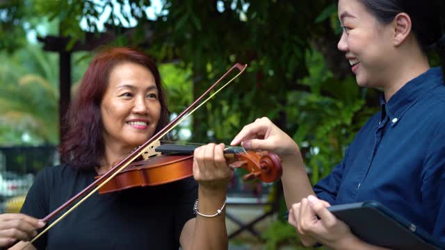 年轻的亚洲妇女教她的母亲如何在室外拉小提琴视频素材