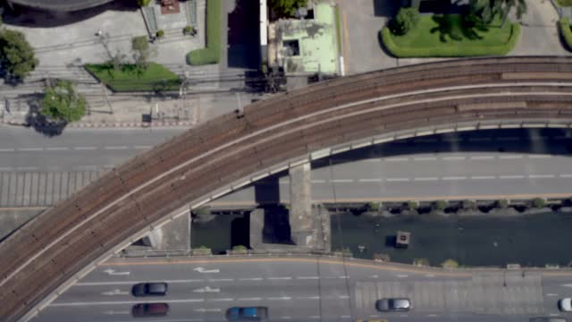 俯视图铁路轻轨与运输轨道交通列车移动在轨道桥上的汽车和车辆行驶在商业城市的地方道路上。视频素材