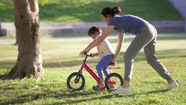 亞洲母親教兒子騎自行車在公園。視頻素材